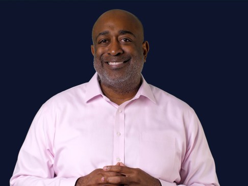 Man in pink shirt standing again navy blue background